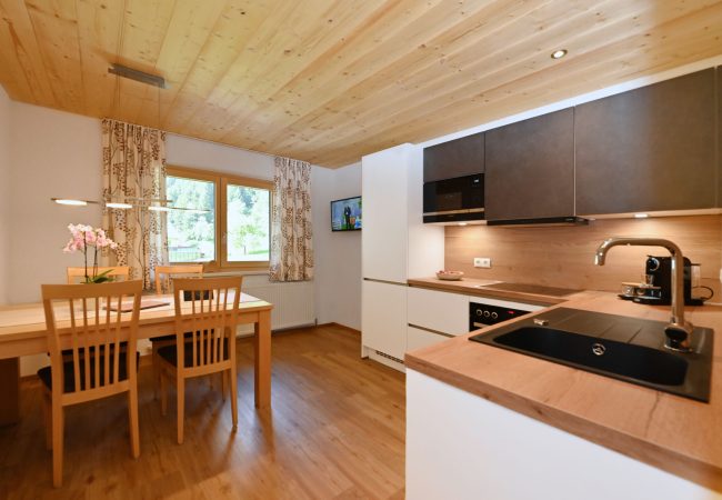 Blick in die helle Küche mit Holztisch und 4 Stühlen auf der linken Seite und der Küchenzeile auf der rechten Seite
