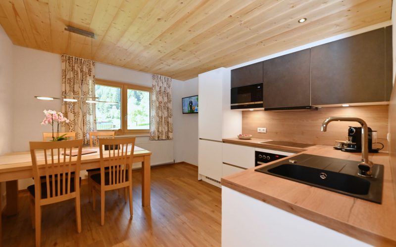 Blick in die helle Küche mit Holztisch und 4 Stühlen auf der linken Seite und der Küchenzeile auf der rechten Seite