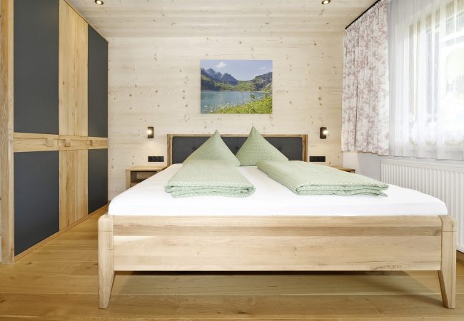 weiteres helles Schlafzimmer mit Doppelbett, Schrank, Holzbdoden, hellem Holz an Decke und Wand mit Fenster