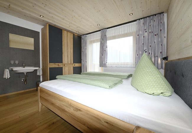 zweites Schlafzimmer mit Doppelbett, Holzboden, Heller Holzverkleidung an Wand und Decke. Dreitüriger Kleiderschrank und Waschbecken mit Spiegel.