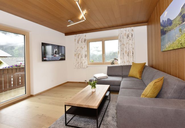 Wohnzimmer mit Holzboden, Sofa und Couchtisch und teils Holzverkleidung an Wand und Zimmerdecke