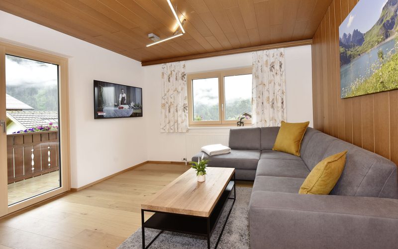 Wohnzimmer mit Holzboden, Sofa und Couchtisch und teils Holzverkleidung an Wand und Zimmerdecke